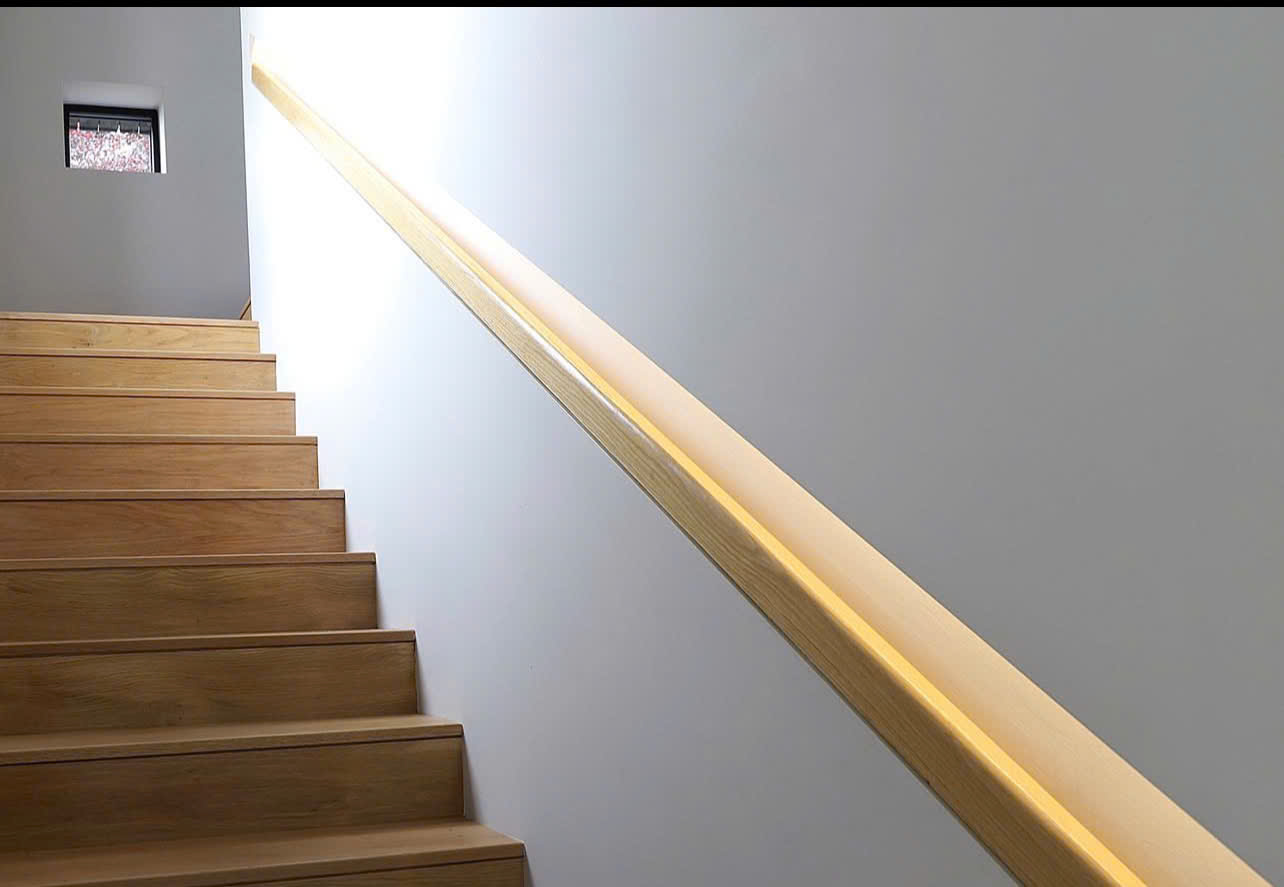 Wooden stair handrail set into the wall with indirect LED lighting