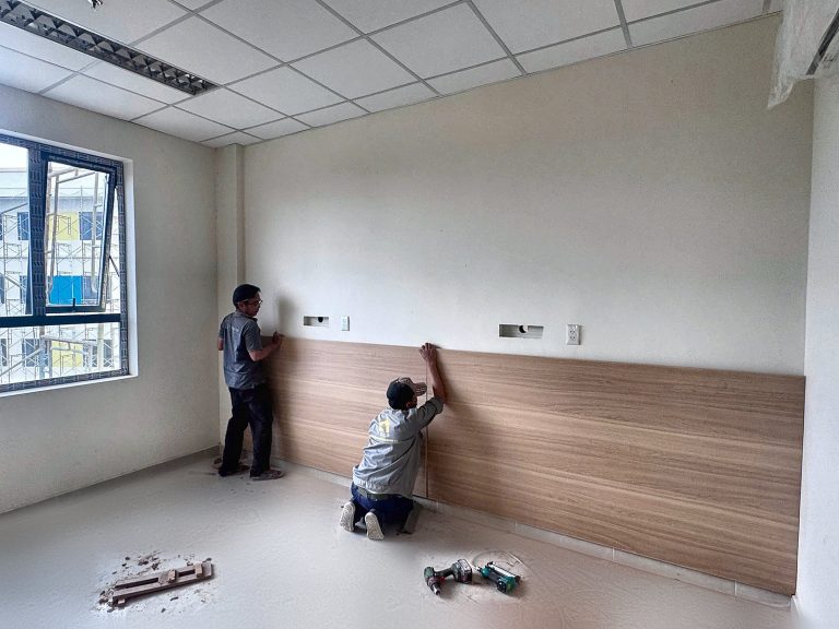 Installing bed-head wall panelling in an inpatient room, Xuyen A Cu Jut Hospital