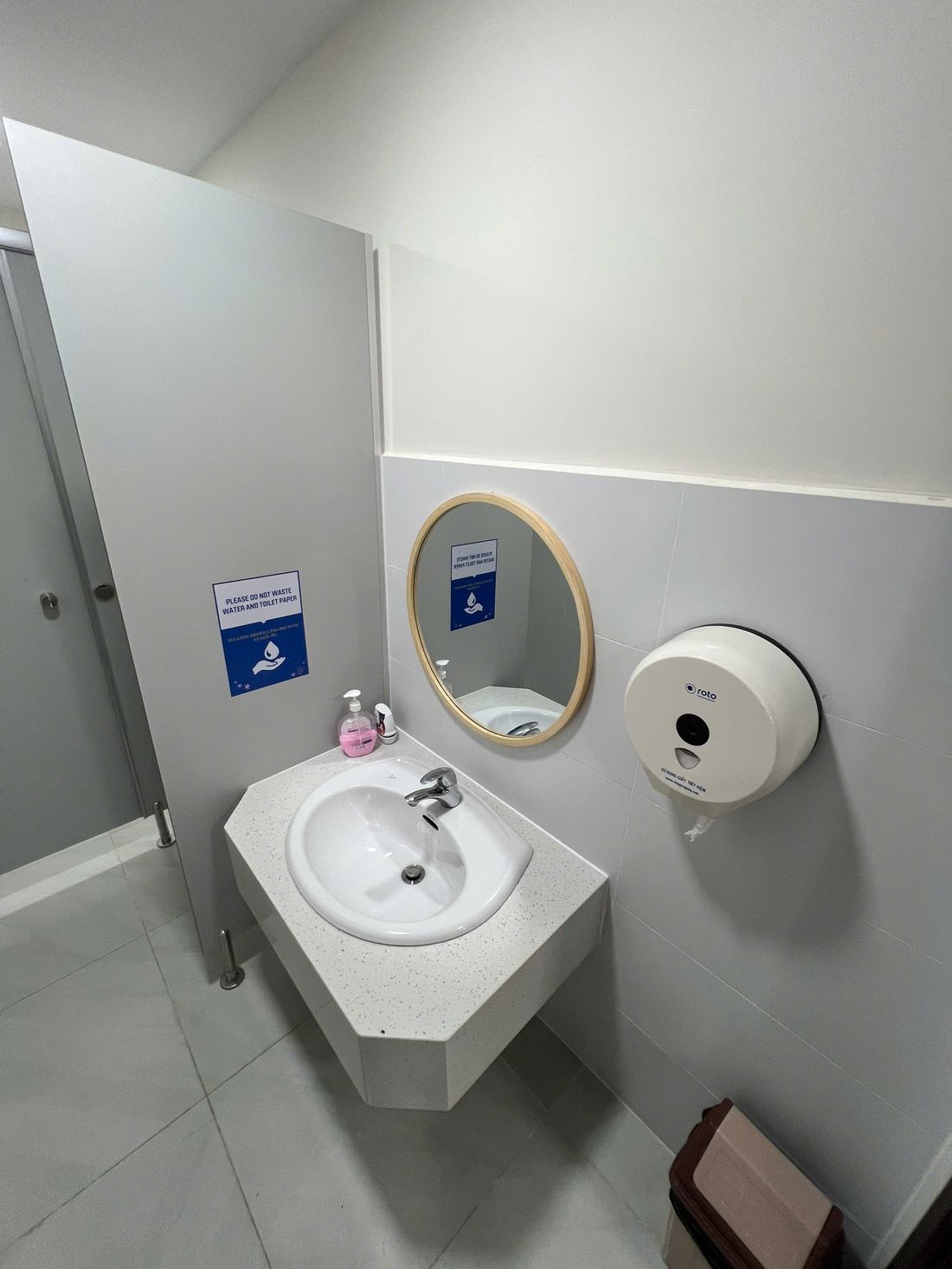 Lavabo đá vát góc mài cạnh, gương khung gỗ và vách ngăn compact chân inox trong nhà vệ sinh trường học